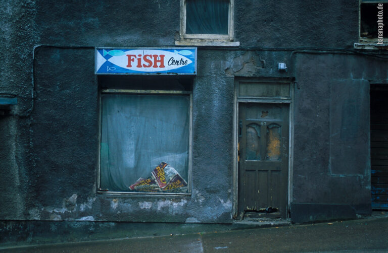 Hauseingang und kleines zugehängtes Schaufenster, völlig heruntergekommene Fassade, Scheiben gesprungen, Leuchtreklame "Fish Center"