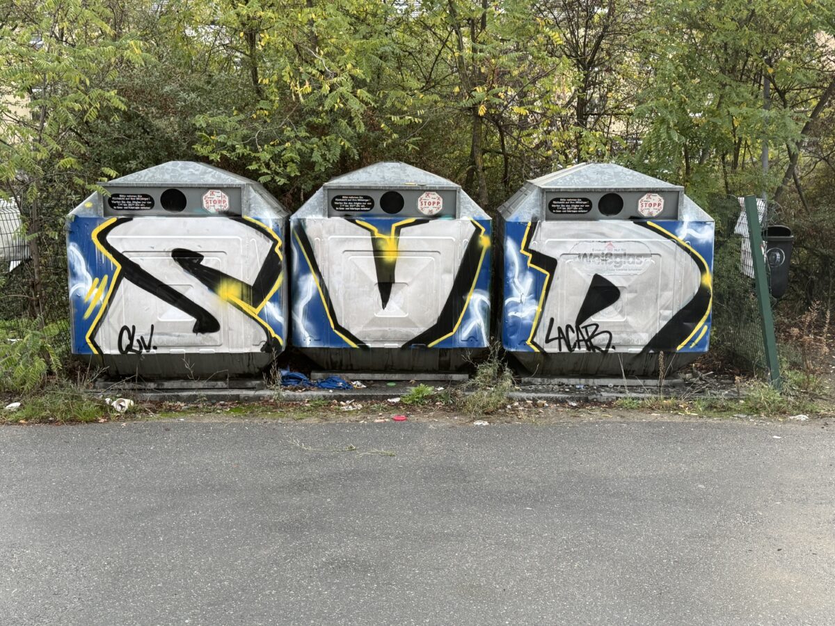 3 Altglascontainer, einer mit einem großen S, die anderen mit V und D beschriftet.
